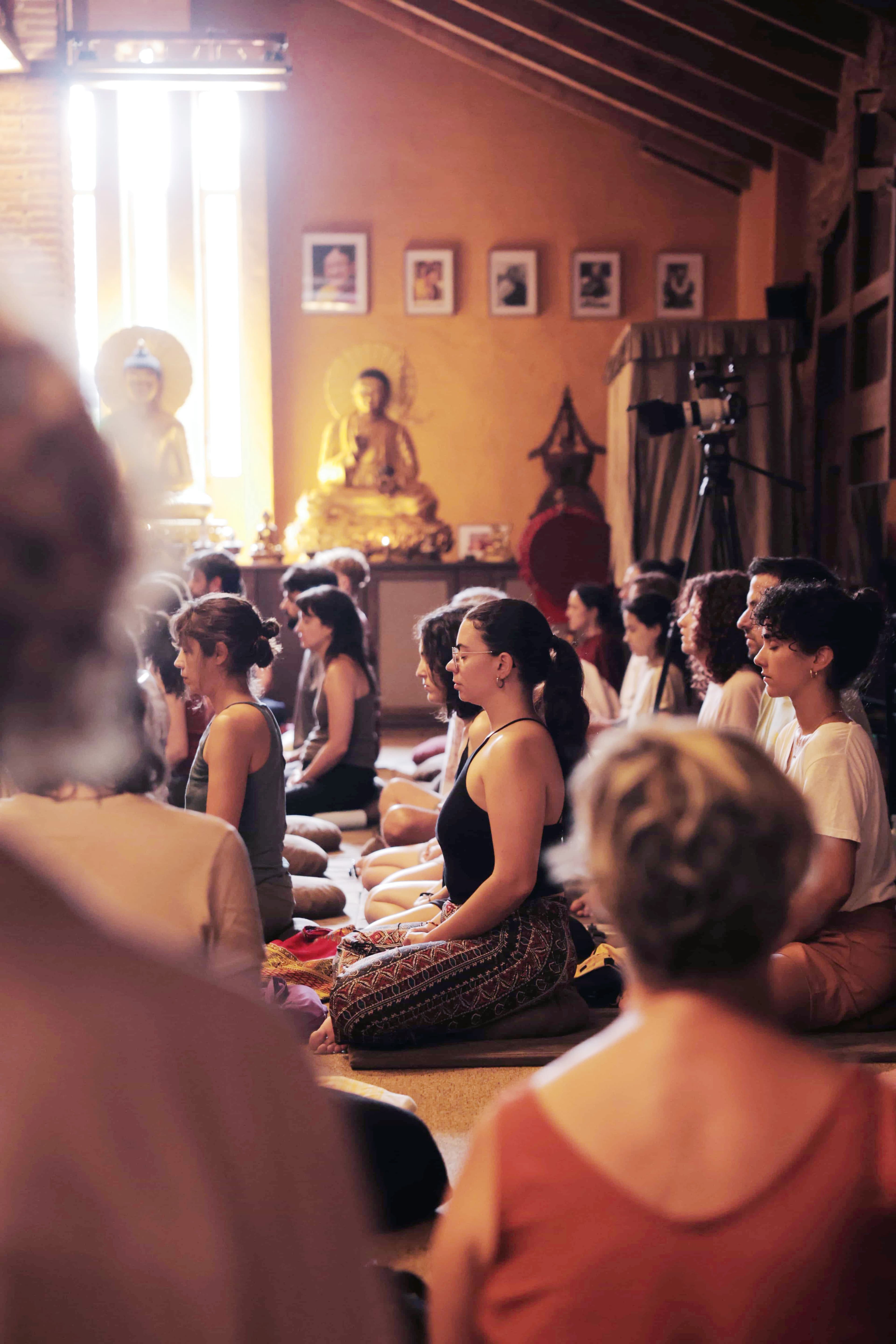 Practitioners meditating in the temple of Casa Virupa during a retreat, with statues in the background