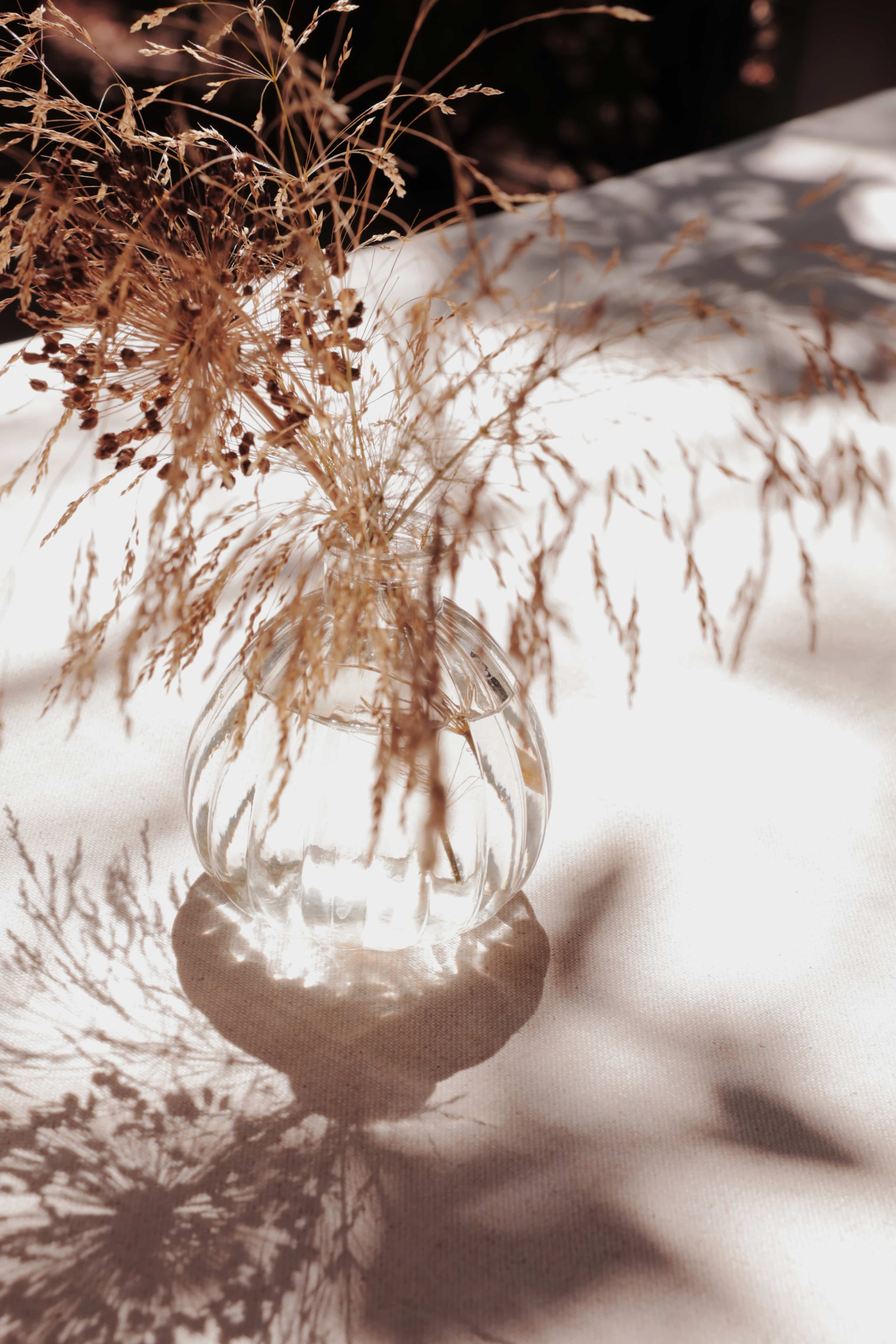 Spherical vase with dried flowers on a table with a white tablecloth.