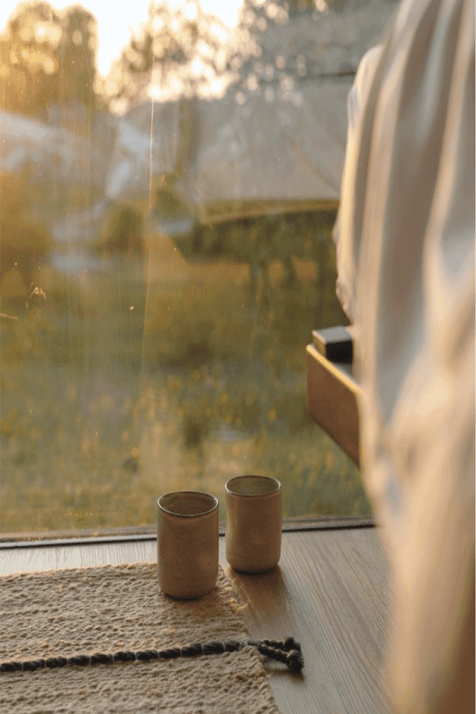 Two cups of tea beside a window overlooking the countryside at sunset