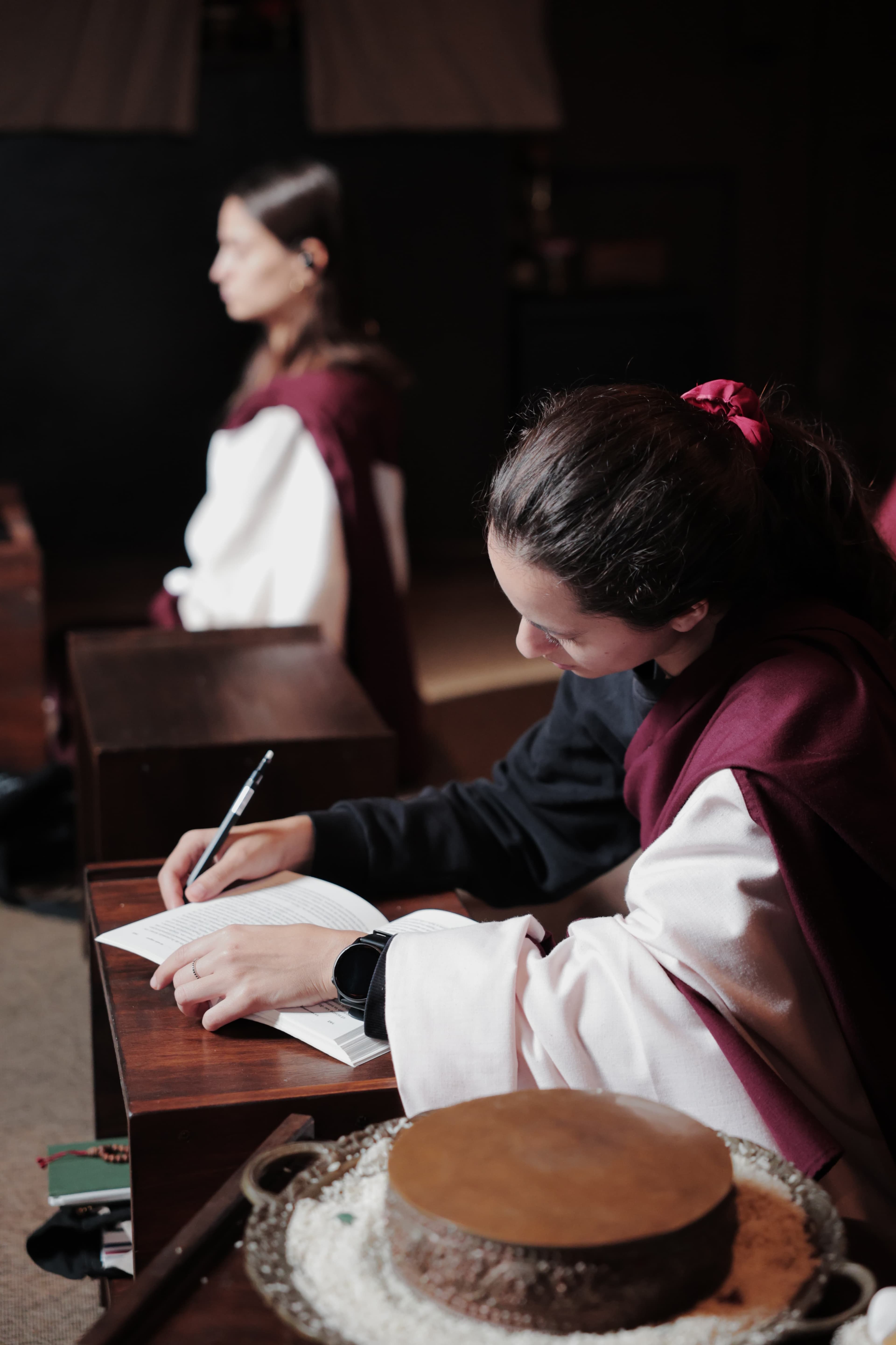 Two people from the community in the temple, one meditating and the other writing in a notebook